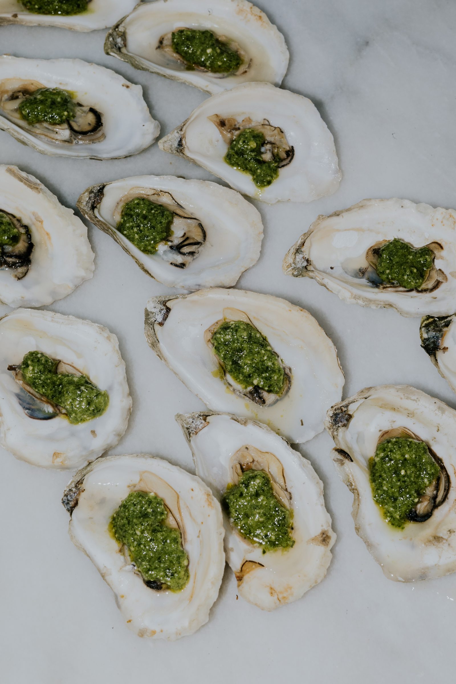 Raw oysters on the half shell, each topped with a spoonful of pesto